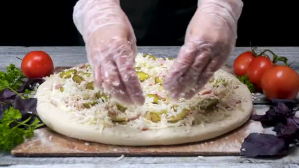 シェフはすりおろしたチーズでピザを振りかけます。フレーム。手袋のプロのピッツェリアシェフは、黒の背景にチーズの最後の層を置きます — ストック動画