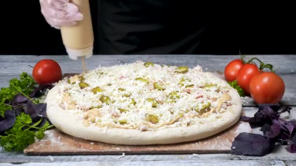 Chef wässert Pizzasauce. Rahmen. Profi-Koch in Handschuhen zum Kochen drückt im Kreis aus Tube Pizzasauce auf schwarzem Hintergrund — Stockvideo
