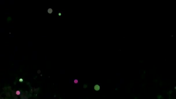 Green and pink glowing glitter particles explosion on black background. Stock footage. Blurred colorful confetti flying in the dark. — Stock Video