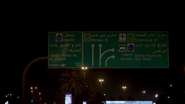 Auf das grüne Verkehrsschild in der Nachtstraße der Vereinigten Arabischen Emirate zusteuern, Reisekonzept. Aktien. Blick aus der Windschutzscheibe eines Autos auf das Verkehrsschild. — Stockvideo