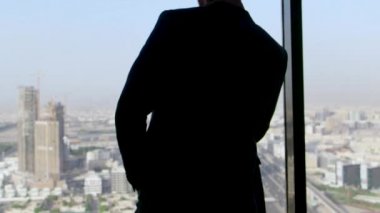 Elinde akıllı telefonuyla ayakta duran takım elbiseli bir işadamının arka dansı, pencereden dışarı bakıyor. Stok. Pencerede şirket lideri, gökdelenden şehre bakış.