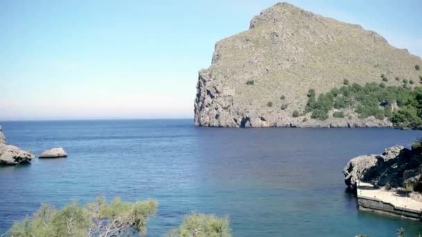 Vista pitoresca do mar azul e da costa rochosa da montanha verde. Arte. Bela paisagem marinha com penhascos rochosos cobertos de vegetação verde e com azul marinho contra o céu azul claro — Vídeo de Stock