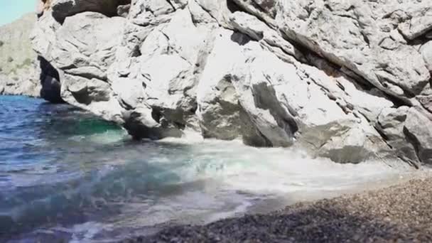 Azul pequeñas olas rompen en rocas y arena de playa. Art. Primer plano de pequeñas olas costeras rodando sobre la arena, rompiendo con rocas al sol. Mar, olas azules y cálido sol de verano son las mejores vacaciones — Vídeo de stock