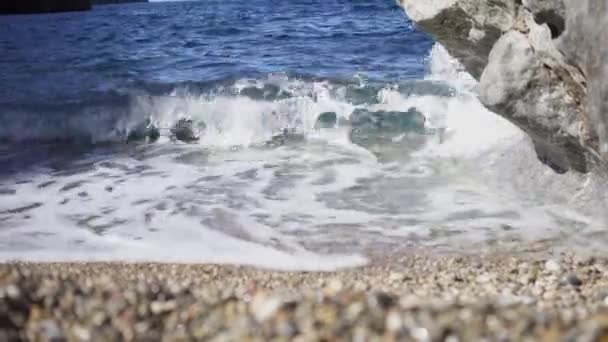 Close-up van kleine golven op zandstrand met rotsen. Kunst. Prachtige blauwe golven breken met wit schuim op zanderige kust en rotsachtige klif. Schoonheid en vrede in blauwe water golven — Stockvideo