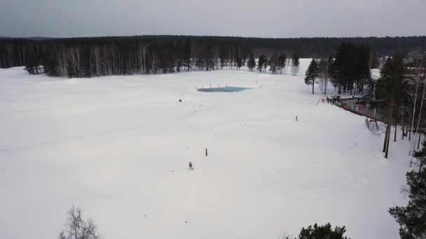 Vista aérea de la estación de esquí con una ruta de esquí y un hombre que participa en la competición de invierno, Rusia. Filmación. Hermosa naturaleza, bosque de pinos y cielo gris pesado . — Vídeos de Stock