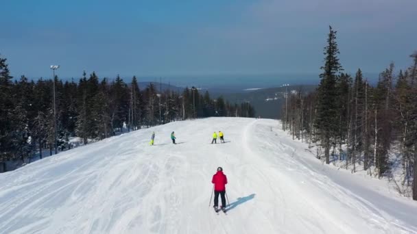 Estância de esqui moderna em aeria floresta de pinheiros, vista de cima. Filmagem. Jovens grupo de pessoas snowboard e esqui descendo a encosta nevada . — Vídeo de Stock