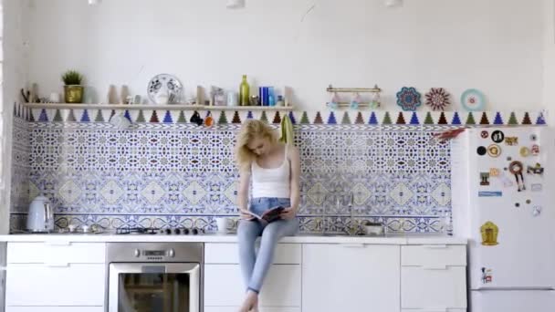 Morgens in der Zeitung blättern. Aktion. schöne fröhliche junge Frau beim Zeitschriftenlesen, während sie zu Hause in der Küche sitzt — Stockvideo
