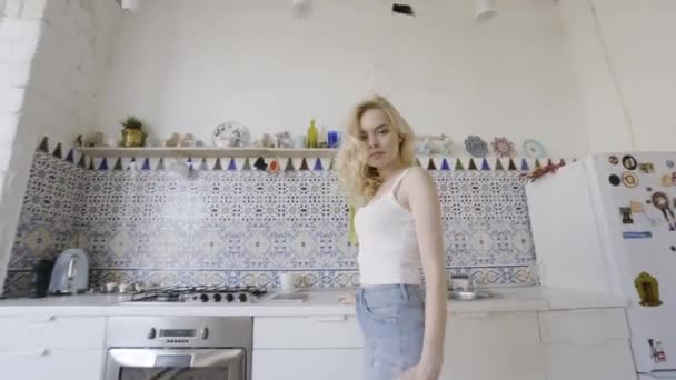 Retrato sexy de jovem loira na cozinha moderna. Acção. Loira sexy na cozinha olha para a câmera de pé — Vídeo de Stock