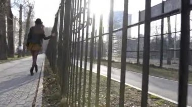 Güneşli bir günde sokakta yürüyen güzel genç kadın. Eylem. Moda genç kadın çit boyunca yürüyüş