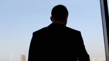 Mavi gökyüzü arka plan üzerinde pencereden şehre bakan işadamı. Stok. Takım elbiseli adam düşünerek ve pencerenin yanındaki bir gökdelenin ofisinde duruyor..