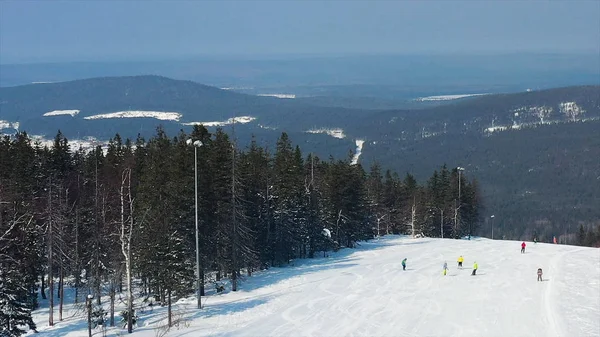 Панорамний вид на спортивний курорт для зимових канікул, концепція здорового способу життя. Кадри. Люди катаються на сноуборді та лижах на пагорбі на зимовому фоні лісу . — стокове фото