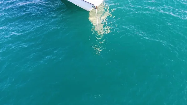 La nariz de un pequeño yate de vela amarrado con una cuerda blanca en el puerto. Acciones. La parte delantera del yate blanco sobre fondo de superficie de mar tranquilo turquesa . — Foto de Stock