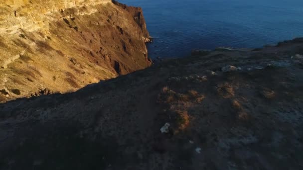 Flygbild över klippa klippa och det omgivande havsvattnet i Sunset Sky. Skott. Brant sluttning av berg nära det lugna havet, naturens skönhet. — Stockvideo