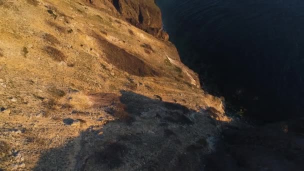 Aerial view of rock cliff and the surrounding sea water in sunset sky. Shot. Steep slope of mountain near the calm sea , beauty of nature. — Stock Video
