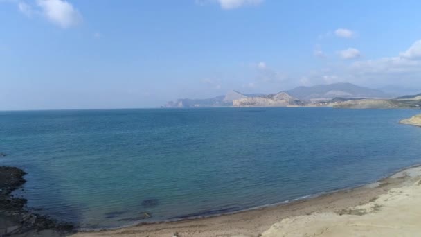 Aerea per una spiaggia sabbiosa, acque blu intenso del Mar Mediterraneo con piccole onde. Gli hanno sparato. Paesaggio marino con montagne all'orizzonte e su sfondo cielo blu . — Video Stock