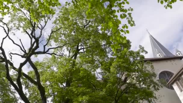 Iglesia y árbol verde en Europa. Acción. La torre de la iglesia parroquial detrás de árboles verdes a principios de primavera — Vídeos de Stock