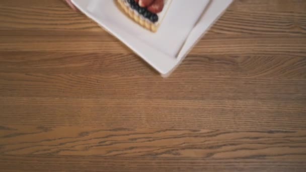 Podrobný pohled na ruce držící bílou misku s lahodné tvarohový koláč, pokrytý borůvkami, ostružinami a jahodami a položením na stůl. Akce. Chutný dort — Stock video