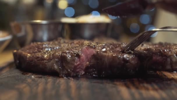 Gros plan sur un steak chaud et savoureux coupé au couteau sur une planche de bois. L'action. Moyenne Rare degré de cuisson du steak — Video