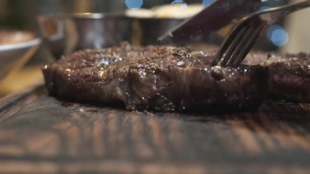 Nahaufnahme von heißen, schmackhaften Steaks, die mit einem Messer auf einem Holzbrett geschnitten werden. Aktion. mittlerer seltener Grad an Steak-Dondness — Stockvideo