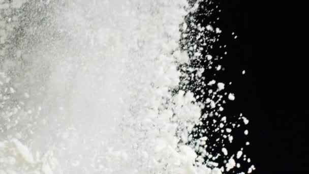 Close-up view of white flakes of powder flying on the black background. Stock footage. Contrast of white and black — Stock Video