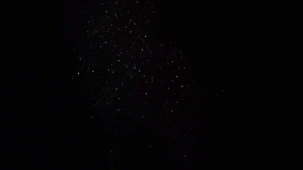 Close-up van sprankelende kleurrijke deeltjes die op de zwarte achtergrond vliegen en glinsteren in het donker. Stock footage. Prachtig uitzicht in het donker — Stockvideo