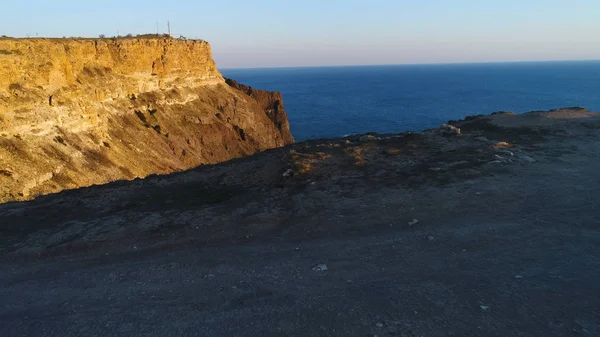 Flygbild över klippa klippa och det omgivande havsvattnet i Sunset Sky. Skott. Brant sluttning av berg nära det lugna havet, naturens skönhet. — Stockfoto