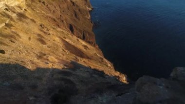 Gün batımında kayalık sakin okyanus sahilinin havadan görünümü. Atış. Okyanus yüzeyinde uçurumun kenarından güzel manzara.