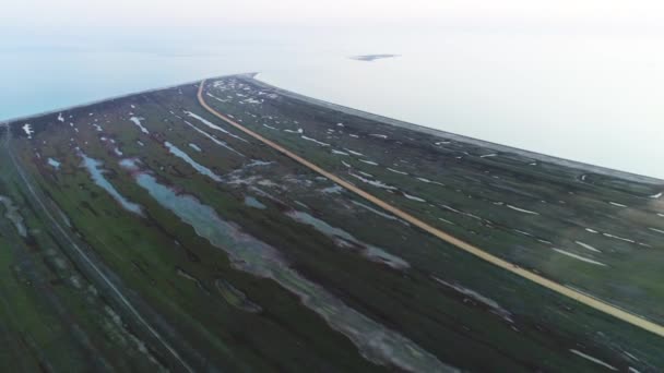 Din partea de sus a unui câmp de pajiști lângă malul mării și un drum galben de țară. Împuşcat. Aeriană pentru un câmp verde inundat abandonat într-o zi tulbure . — Videoclip de stoc