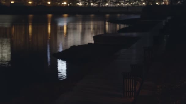 川の近くの空のアスファルト歩道、夜の都市。ストック映像。堤防のある美しい夜の街の風景、川の近くのベンチ. — ストック動画