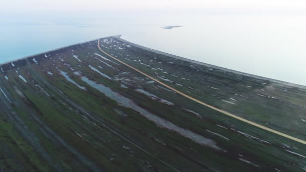 From above view of a meadow field near the sea shore and a yellow country road. Shot. Aerial for a abandoned flooded green field in a cloudy day. — Αρχείο Βίντεο