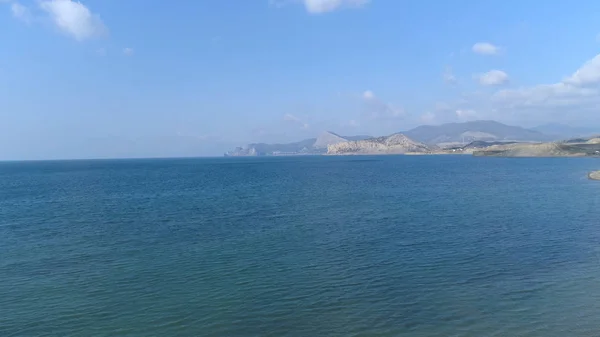 Antenn för en sandstrand, djupt blått vatten i Medelhavet med små vågor. Skott. Seascape med berg vid horisonten och på blå himmel bakgrund. — Stockfoto