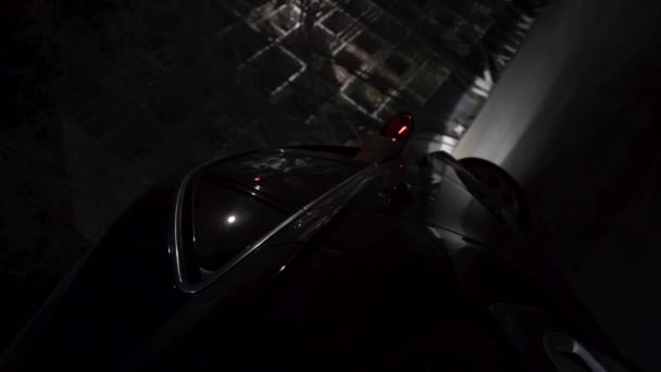 Primer plano para el coche negro que se mueve en la ciudad por la noche con diferentes luces brillantes, concepto de vida nocturna. Filmación. Vista desde la rueda de un coche moderno negro en la calle . — Vídeo de stock