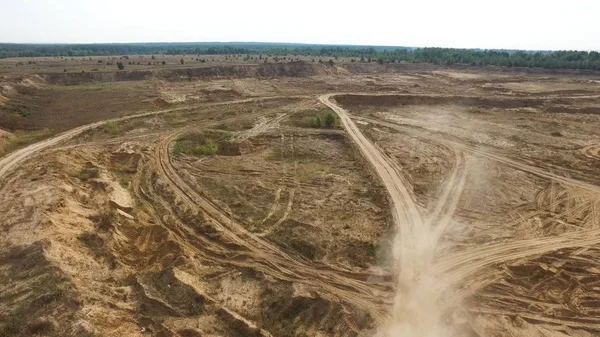 Aerial for the earth quarry with many tire tracks and the dust flying above the ground. Stock footage. Industrial landscape with truck tracks on the dry ground in a sunny day.