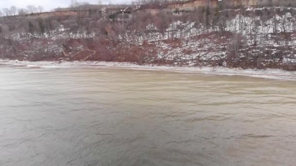Vue aérienne de la rivière large et le rivage enneigé avec des arbres poussant sur la colline, la nature en hiver. Des actions. Paysage hivernal avec rivière jaune froid et montagne boisée .