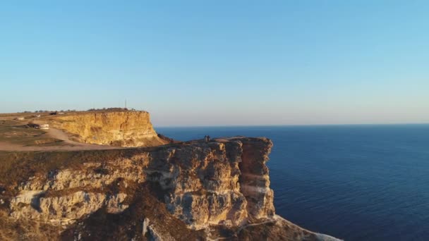 Aerial view of people standing on a large cliff against blue clear sky and blue sea water. Shot. Beautiful view from above — Stock Video