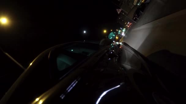 Achteraanzicht van een zwarte auto die door donkere nacht stad beweegt en begint te parkeren, nacht verkeers concept. Beelden. Personenauto met neon glinsterende verlichting parkeren in de straat. — Stockvideo