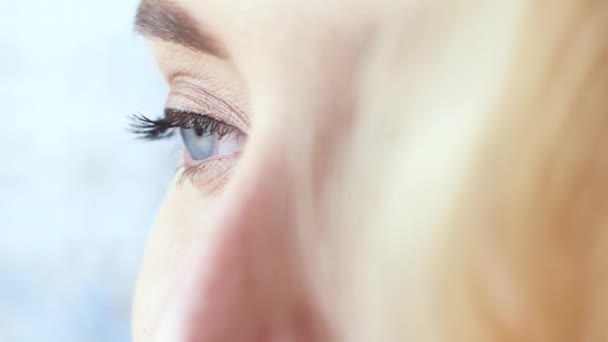 Vista da vicino della bella giovane donna viso con perfetto trucco nudo, che sta mettendo in evidenza gli occhi occhi occhi azzurri e capelli biondi. Azione. Concetto immagini donne — Video Stock