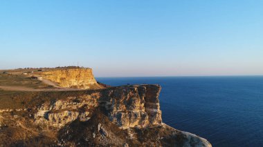 Mavi berrak gökyüzü ve mavi deniz suyuna karşı büyük bir uçurumun üzerinde duran insanların havadan görünümü. Atış. Yukarıdan güzel manzara