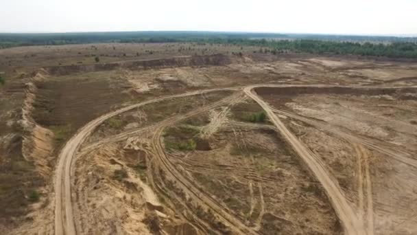 多くのタイヤトラックと地面の上を飛ぶほこりと地球採石場のための空中。ストック映像。晴れた日の乾燥した地面にトラックのトラックトラックと産業風景. — ストック動画