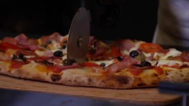 Şeflerin elleri siyah koruyucu eldivenlerle mutfakta pastırma ve domatesli taze lezzetli bir pizza yıkıyor. Çerçeve. Geleneksel İtalyan Yemekleri