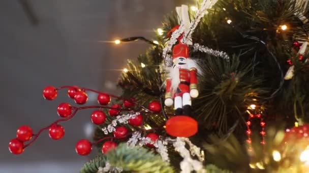 Vista dal basso della tradizionale statuetta degli schiaccianoci in abito rosso appesa ad un albero di Natale vicino alle luci e ad altre decorazioni. Cornice. L'umore di Natale — Video Stock