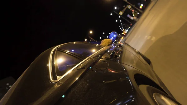 Carro preto rápido dirigindo na estrada da noite através da cidade, vista da roda. Filmagem. Veículo moderno movendo-se ao longo da movimentada cidade à noite, conceito de viagem rodoviária . — Fotografia de Stock