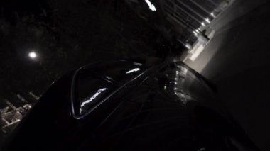 Farklı parlayan ışıklar, gece hayatı kavramı ile gece şehirde park siyah araba için kapatın. Görüntü. Sokakta siyah modern bir arabanın tekerleğinden görünüm.