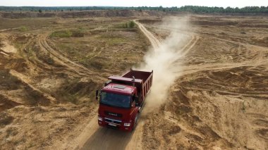 Toz bulutları ile kuru kırsal yolda sürüş büyük kırmızı kamyon iki adam için anten. Sahne. Arka planda yeşilçam ormanı bulunan kuru zemin ocağında hareket eden kamyon.