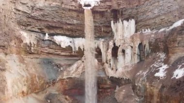 Kayalık yamaçlarda kirli buz ile kayalıklarda aşağı dalan küçük sarı su akışı için anten. Stok. Kirli su düşen yüksek taş ocağıdik eğim, doğal arka plan.