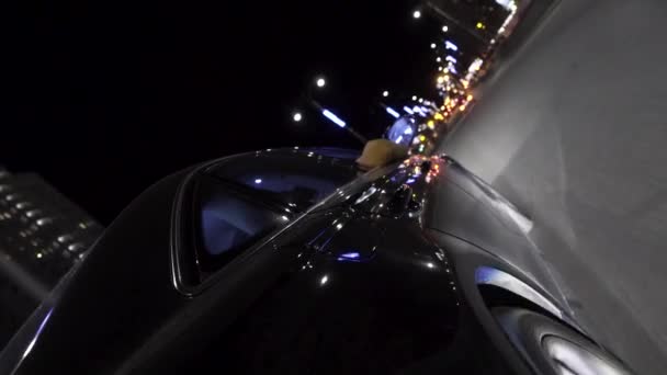 Auto moderna nera che si muove nelle strade della città di notte con auto luci a LED scintillano in diversi colori. Un filmato. L'auto che guida sullo sfondo di edifici di sera . — Video Stock