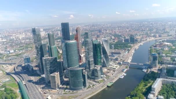 Blick von oben auf das Business Center mit Wolkenkratzern im Hintergrund des Stadtpanoramas. Aktion. Stadtbild mit atemberaubenden Ausblicken auf verspiegelte Wolkenkratzer vor blauem Himmel und Fluss — Stockvideo