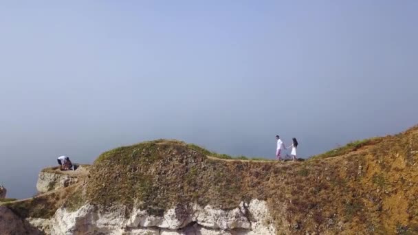 Toppen utsikt över par promenader längs Cliff Path. Åtgärder. Ungt par i kärlek går längs smala stigen i varm sommar på bakgrund gråaktig Horisont — Stockvideo