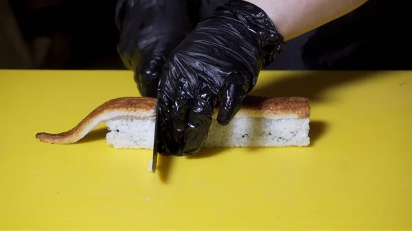 Gros plan pour couteau à la main en coupant le rouleau sur un carton jaune, la nourriture asiatique et le concept de cuisson. Cadre. Gros plan pour les mains de chef coupant le rouleau préparé en morceaux . — Photo