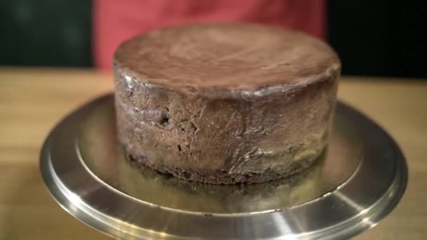 Primer plano de chocolate líquido vertido en la torta. Acción. El chocolate líquido derretido se extiende sobre el pastel redondo en el soporte de hierro. Pastel de cobertura con jarabe de chocolate. Artículos de confitería y pastelería — Vídeo de stock